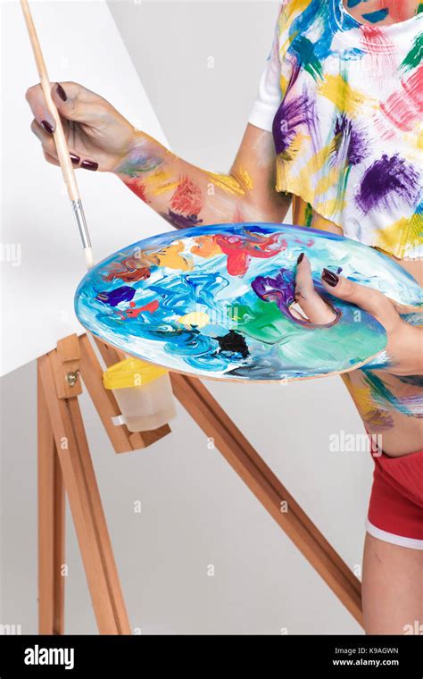 An artist holding a wooden palette, with paints and brushes nearby