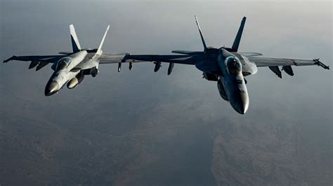 F/A-18 Hornets flying in formation over a cloudy landscape